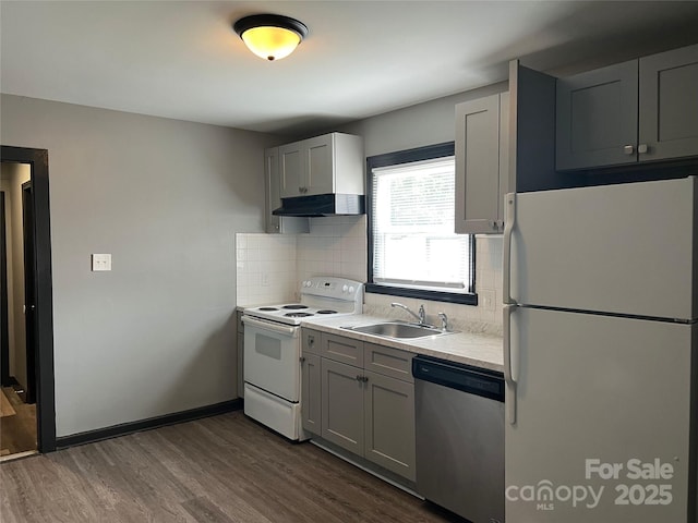 kitchen with sink, gray cabinetry, dark hardwood / wood-style floors, white appliances, and decorative backsplash