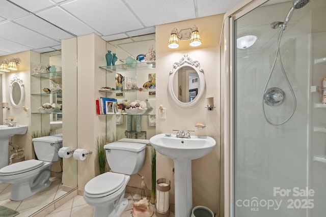 bathroom with tile patterned flooring, a paneled ceiling, a shower with shower door, and toilet