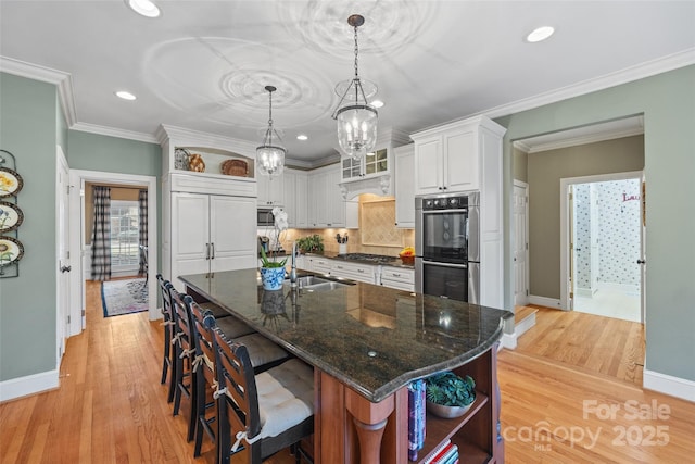 kitchen featuring appliances with stainless steel finishes, white cabinetry, sink, light wood-type flooring, and dark stone counters