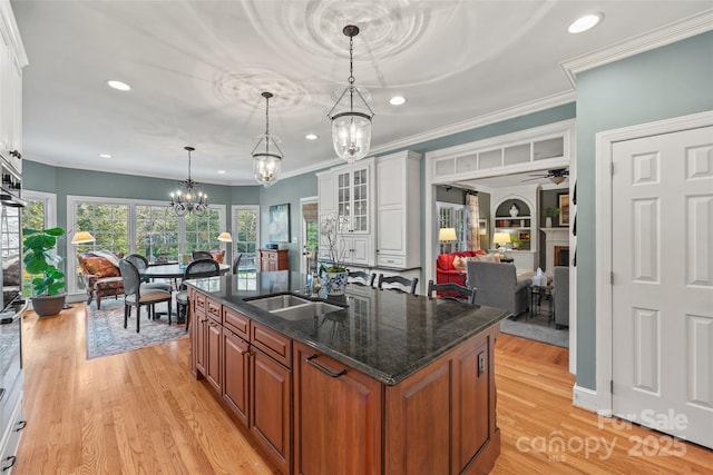 kitchen featuring white cabinetry, dark stone counters, sink, pendant lighting, and an island with sink