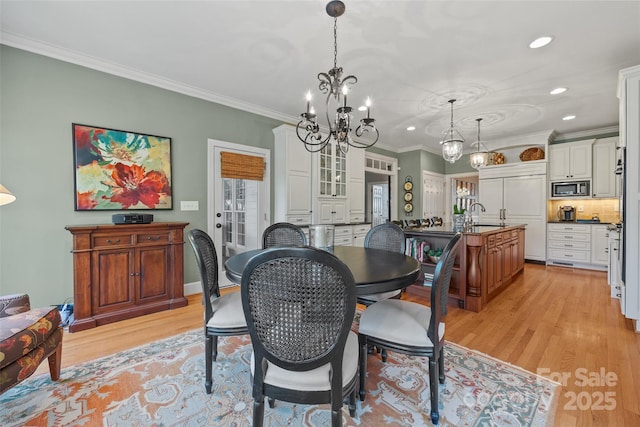 dining space with light wood-type flooring, a chandelier, ornamental molding, and sink