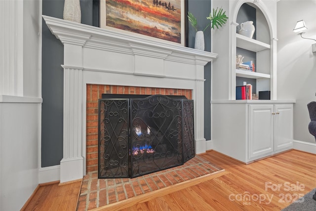 room details with a brick fireplace, built in shelves, and hardwood / wood-style floors