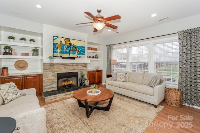 living room featuring a fireplace, built in features, a wealth of natural light, and light hardwood / wood-style floors