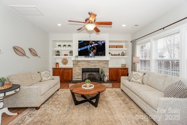 living room with built in shelves, a fireplace, and light hardwood / wood-style floors