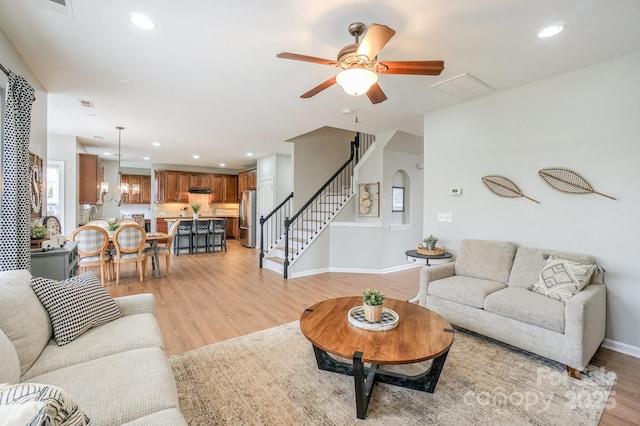 living room featuring ceiling fan with notable chandelier and light hardwood / wood-style floors