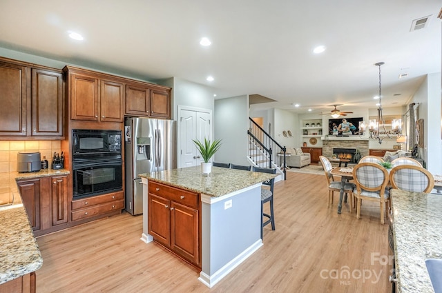 kitchen with a kitchen island, decorative light fixtures, light stone counters, and black appliances