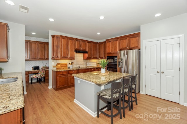 kitchen with a center island, light hardwood / wood-style floors, light stone countertops, and black appliances