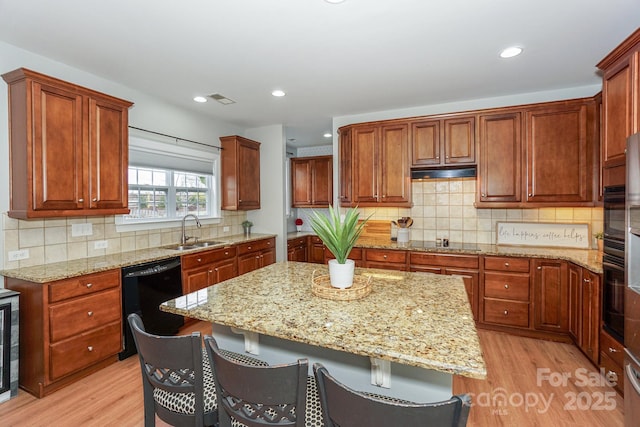 kitchen featuring sink, light hardwood / wood-style flooring, a kitchen breakfast bar, light stone countertops, and black appliances