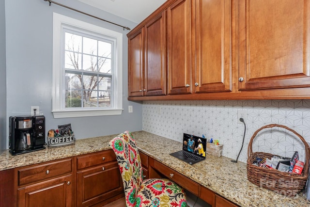 kitchen featuring light stone counters, backsplash, and built in desk