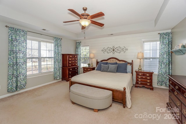 bedroom with ceiling fan, light colored carpet, a raised ceiling, and multiple windows