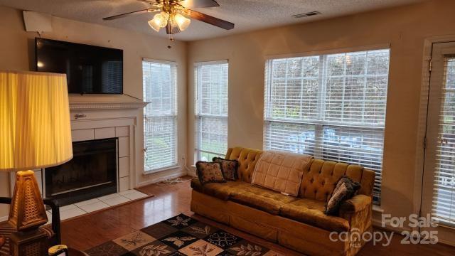 living room featuring a tiled fireplace, hardwood / wood-style flooring, a textured ceiling, and ceiling fan