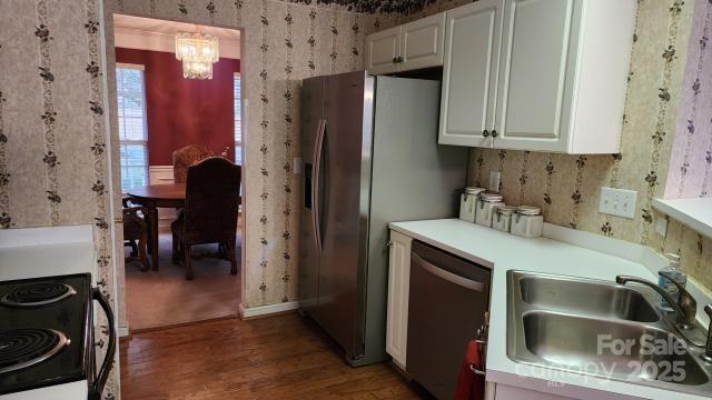 kitchen featuring wood-type flooring, dishwasher, sink, decorative light fixtures, and white cabinets