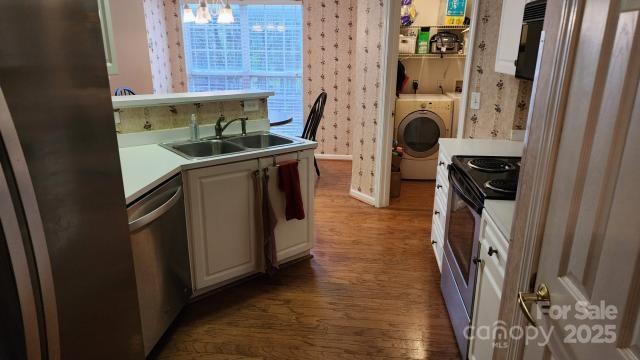 kitchen with washer / clothes dryer, white cabinetry, sink, stainless steel appliances, and dark hardwood / wood-style floors