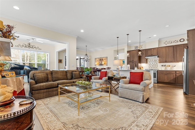 living room featuring ornamental molding, sink, light wood-type flooring, and a notable chandelier