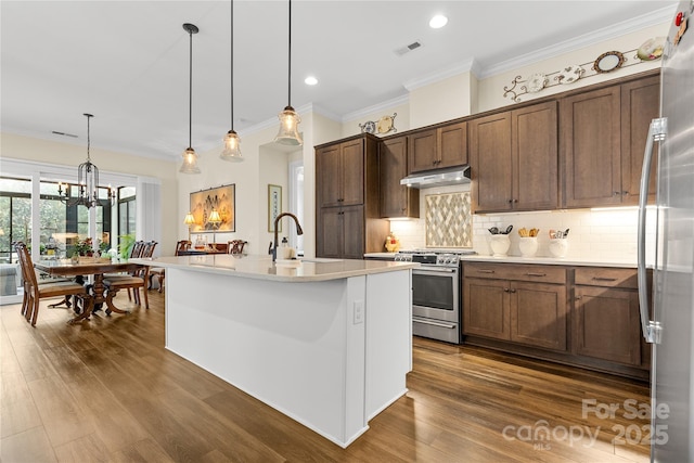 kitchen with hanging light fixtures, stainless steel appliances, sink, and a center island with sink