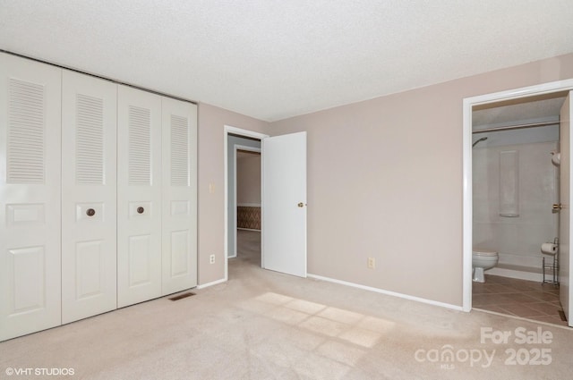 unfurnished bedroom featuring light carpet, ensuite bath, a closet, and a textured ceiling