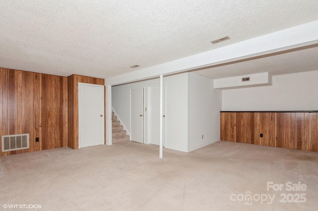 basement featuring light carpet, a textured ceiling, and wood walls