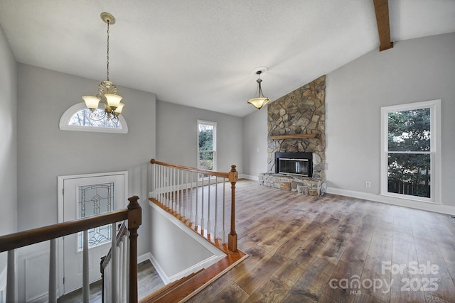 interior space featuring a notable chandelier, hardwood / wood-style flooring, a stone fireplace, and lofted ceiling with beams