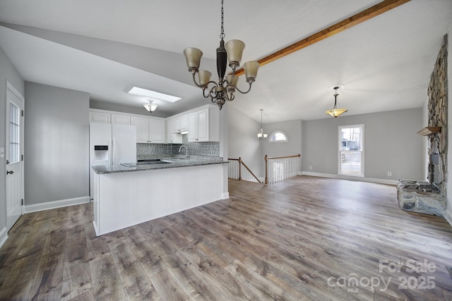 kitchen featuring vaulted ceiling with skylight, tasteful backsplash, white cabinets, white refrigerator with ice dispenser, and a notable chandelier