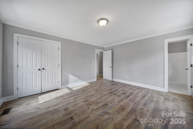 unfurnished bedroom featuring crown molding, a closet, ensuite bathroom, and light hardwood / wood-style flooring