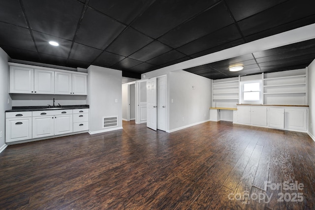 unfurnished living room featuring sink, dark hardwood / wood-style flooring, and built in shelves