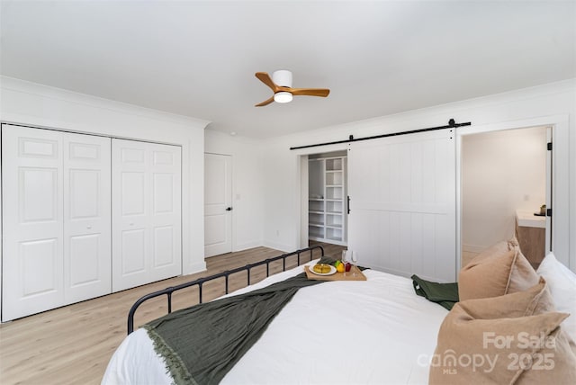 bedroom featuring crown molding, a barn door, a closet, light hardwood / wood-style flooring, and ceiling fan