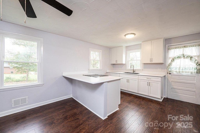 kitchen featuring kitchen peninsula, black electric cooktop, dark hardwood / wood-style flooring, white cabinets, and sink