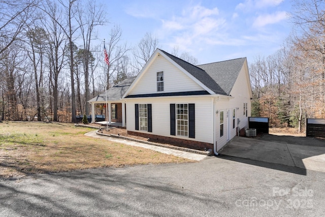 view of home's exterior featuring brick siding, a yard, central air condition unit, a porch, and driveway