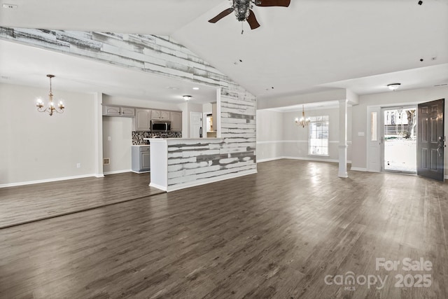 unfurnished living room featuring baseboards, dark wood-style floors, vaulted ceiling, ornate columns, and ceiling fan with notable chandelier