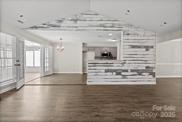 unfurnished living room featuring a chandelier, vaulted ceiling, and dark wood finished floors