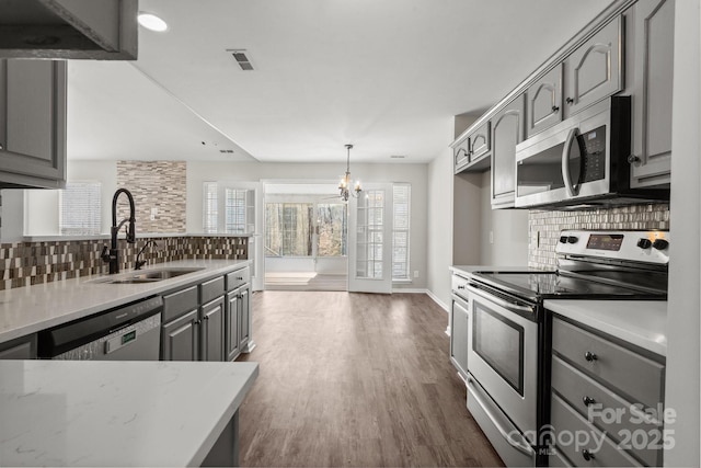 kitchen featuring stainless steel appliances, a sink, decorative backsplash, and gray cabinetry