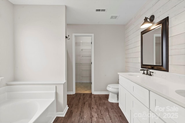 full bathroom featuring a walk in closet, visible vents, a sink, wood finished floors, and a bath