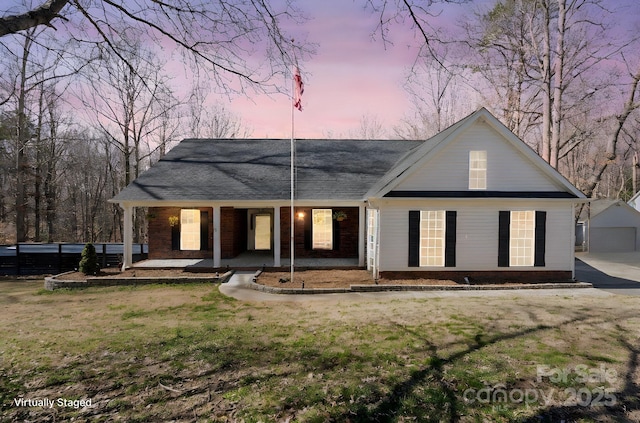 back of property at dusk with brick siding, a porch, and a yard