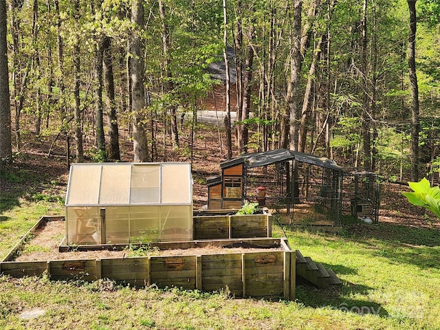 view of yard featuring a garden, a forest view, an outdoor structure, and a greenhouse