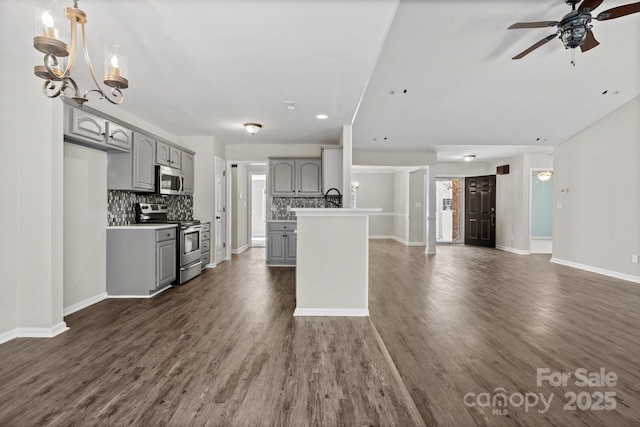 kitchen featuring tasteful backsplash, gray cabinets, open floor plan, stainless steel appliances, and ceiling fan with notable chandelier