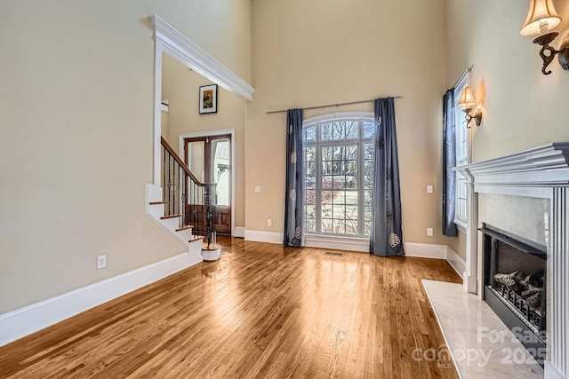 entrance foyer featuring wood-type flooring, a towering ceiling, and a high end fireplace