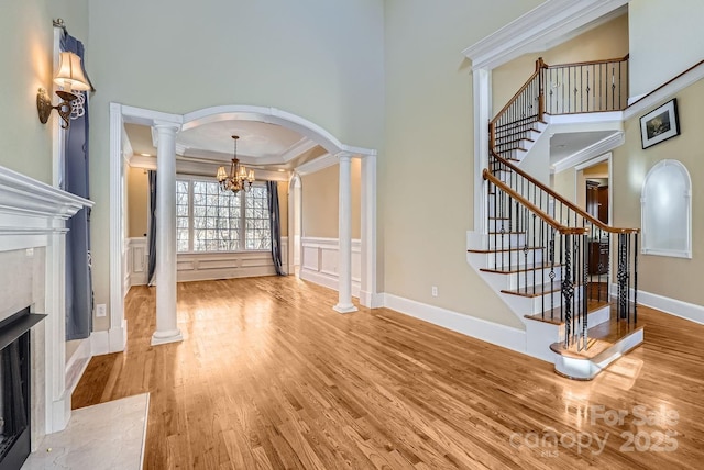 living room featuring ornate columns, wood-type flooring, a chandelier, a high ceiling, and ornamental molding