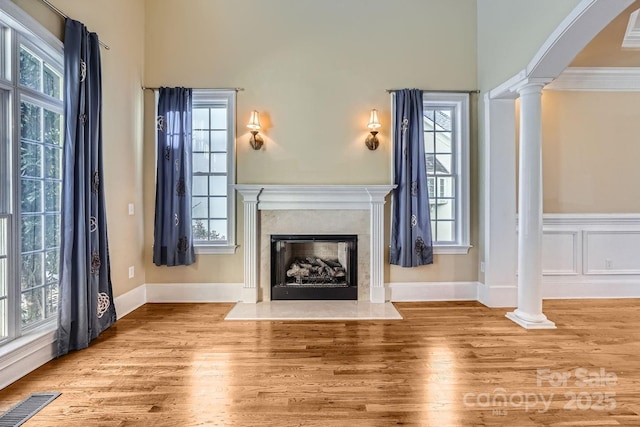 unfurnished living room featuring decorative columns, a high end fireplace, ornamental molding, and a healthy amount of sunlight