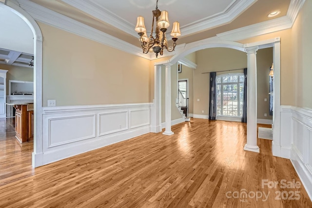 unfurnished dining area featuring crown molding, ornate columns, a notable chandelier, coffered ceiling, and light hardwood / wood-style floors