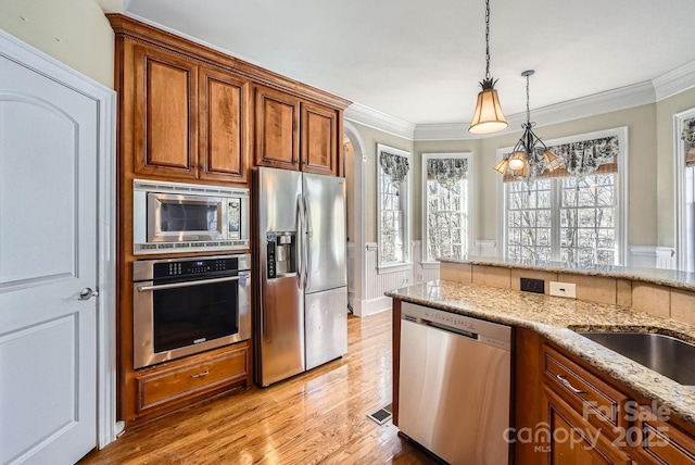 kitchen with ornamental molding, light stone counters, pendant lighting, and appliances with stainless steel finishes