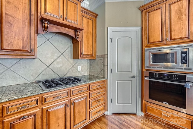 kitchen with appliances with stainless steel finishes, dark stone countertops, decorative backsplash, light hardwood / wood-style floors, and ornamental molding