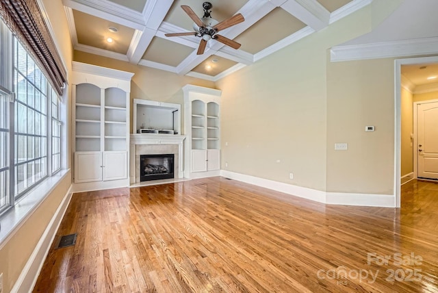 unfurnished living room with built in shelves, coffered ceiling, a healthy amount of sunlight, and beamed ceiling