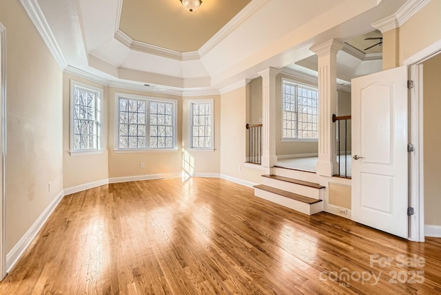 spare room featuring crown molding, ceiling fan, hardwood / wood-style flooring, a tray ceiling, and decorative columns