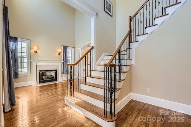 stairs featuring a high ceiling, wood-type flooring, and a premium fireplace