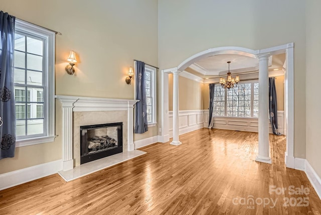 unfurnished living room with decorative columns, a healthy amount of sunlight, ornamental molding, and a fireplace