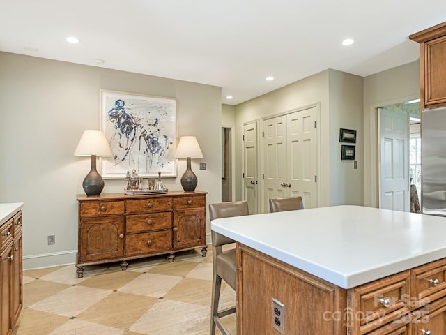 kitchen with baseboards, brown cabinetry, a kitchen island, and recessed lighting