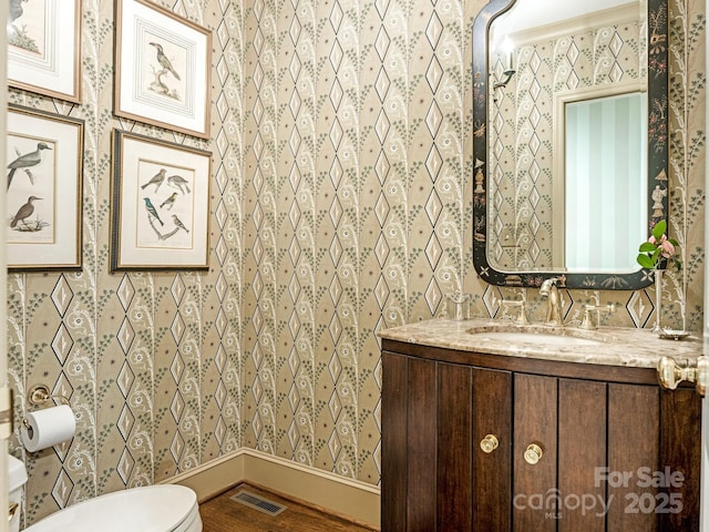 half bath featuring visible vents, toilet, wood finished floors, baseboards, and wallpapered walls