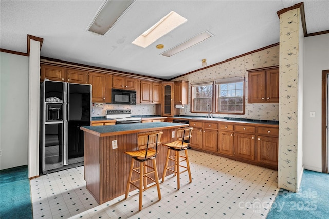 kitchen with a kitchen bar, lofted ceiling with skylight, crown molding, a center island, and black appliances