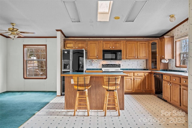 kitchen featuring sink, a kitchen bar, black appliances, ornamental molding, and a kitchen island