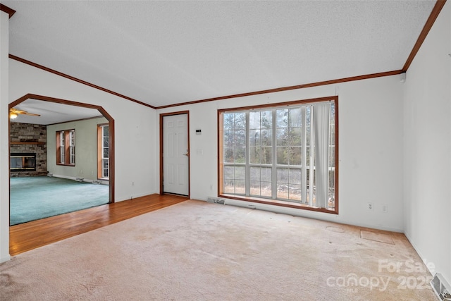 carpeted empty room with crown molding, ceiling fan, a textured ceiling, and a fireplace